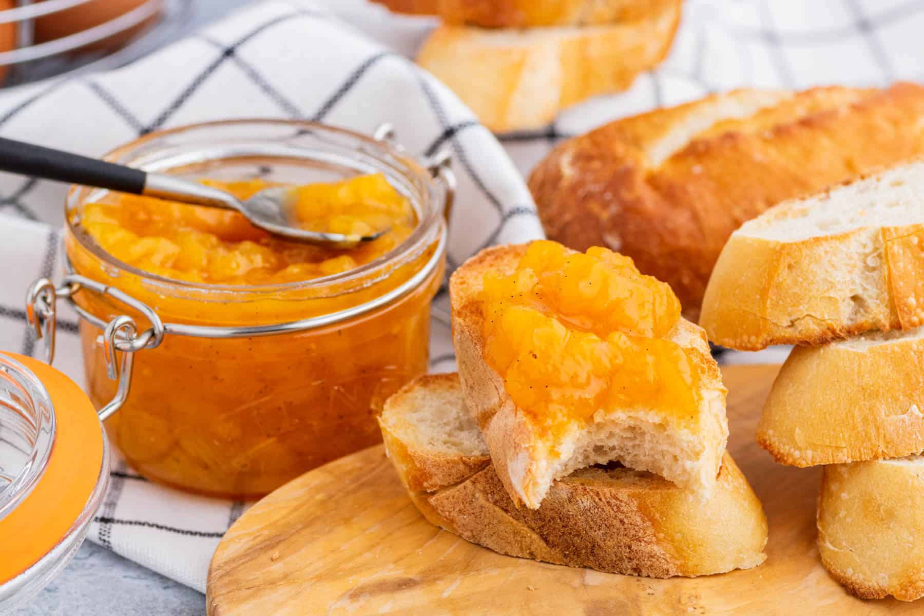 A toast covered in bright orange Peach Freezer Jam in front of a jar of the same jam.