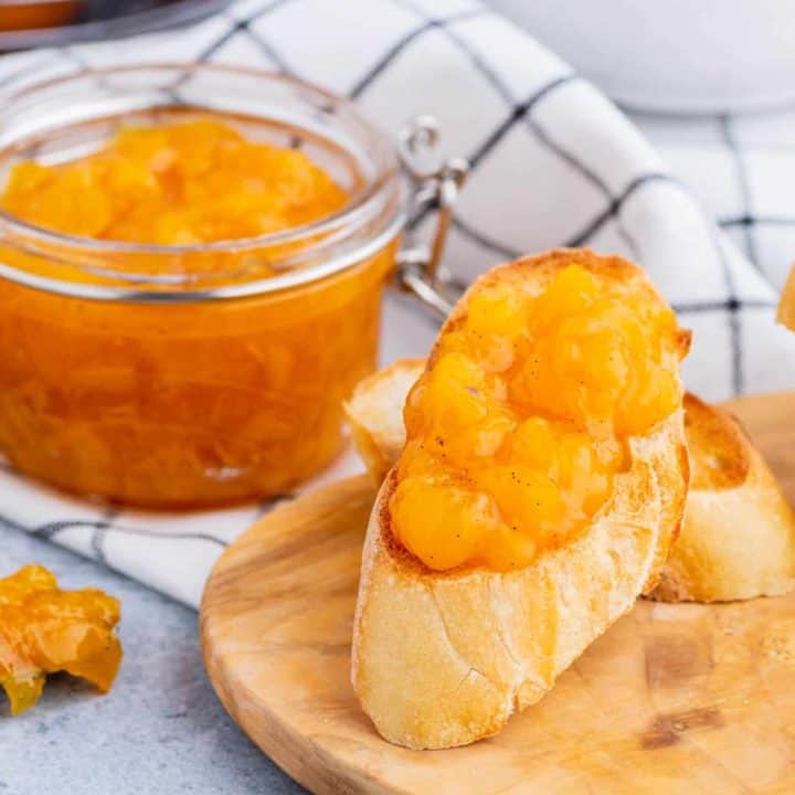 A toast covered in bright orange Peach Freezer Jam in front of a jar of the same jam.