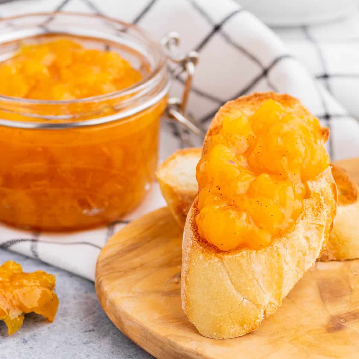 A toast covered in bright orange Peach Freezer Jam in front of a jar of the same jam.