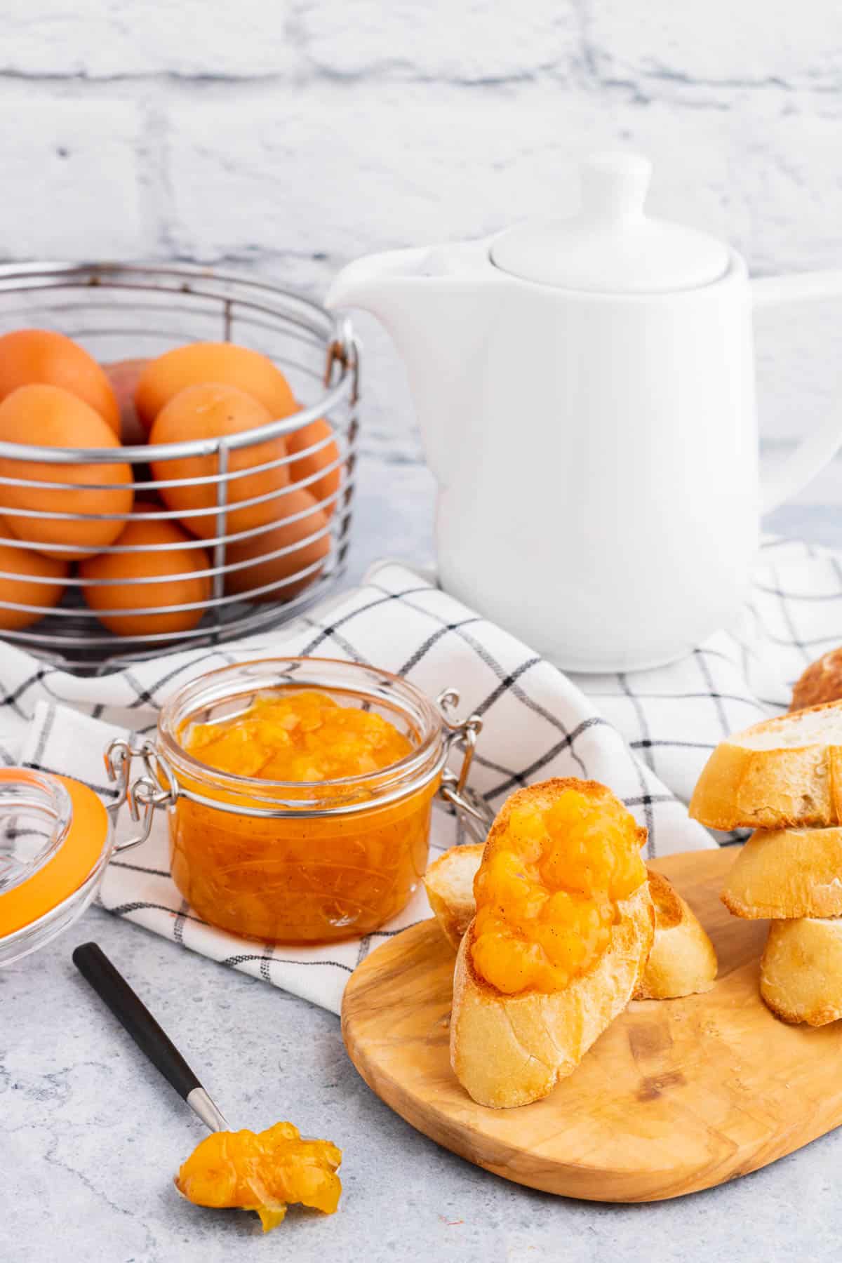 Breakfast scene with a coffee pot, eggs, and toast covered in bright orange Peach Freezer Jam in front of a jar of the same jam.