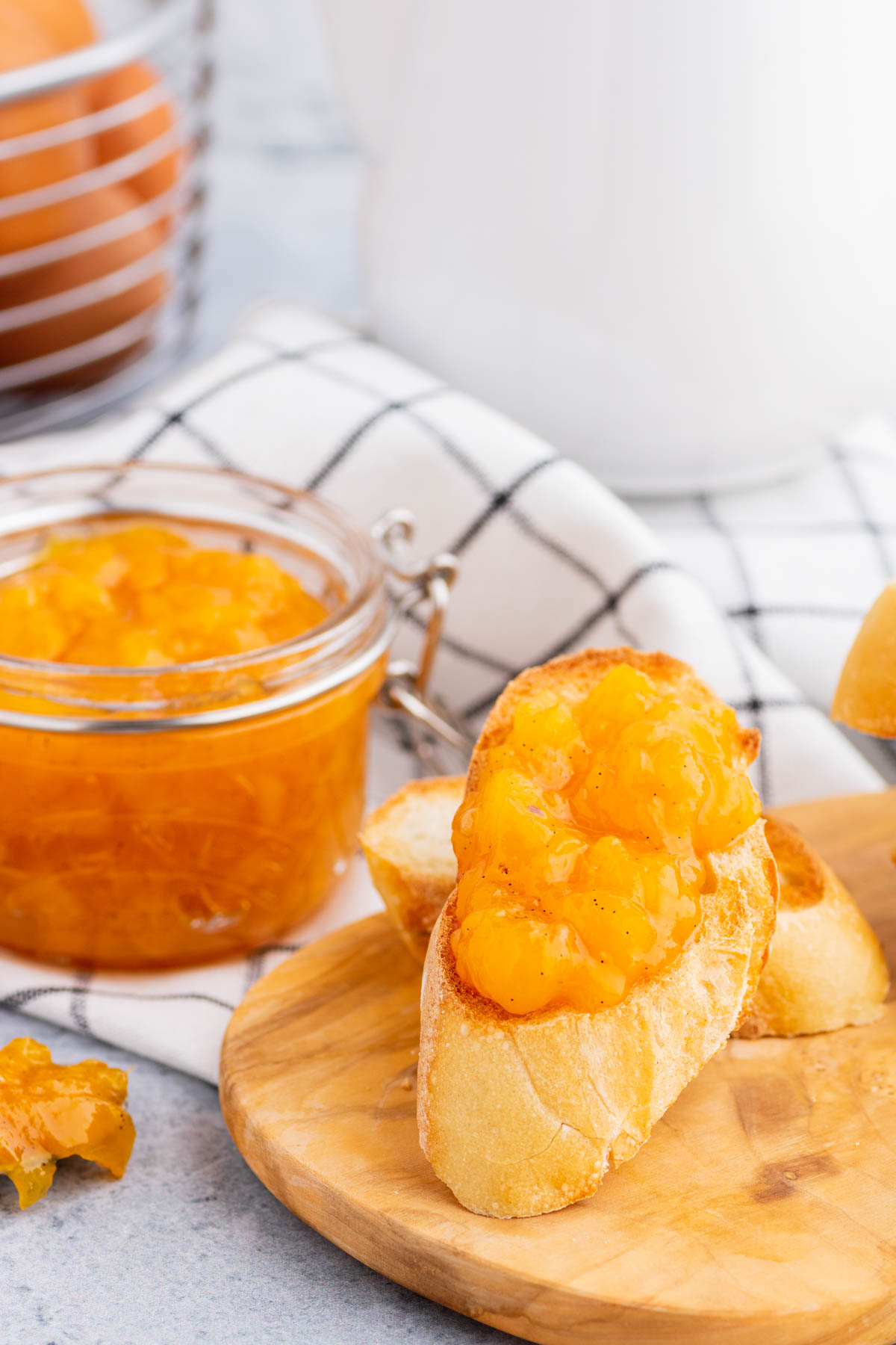 A toast covered in bright orange Peach Freezer Jam in front of a jar of the same jam.