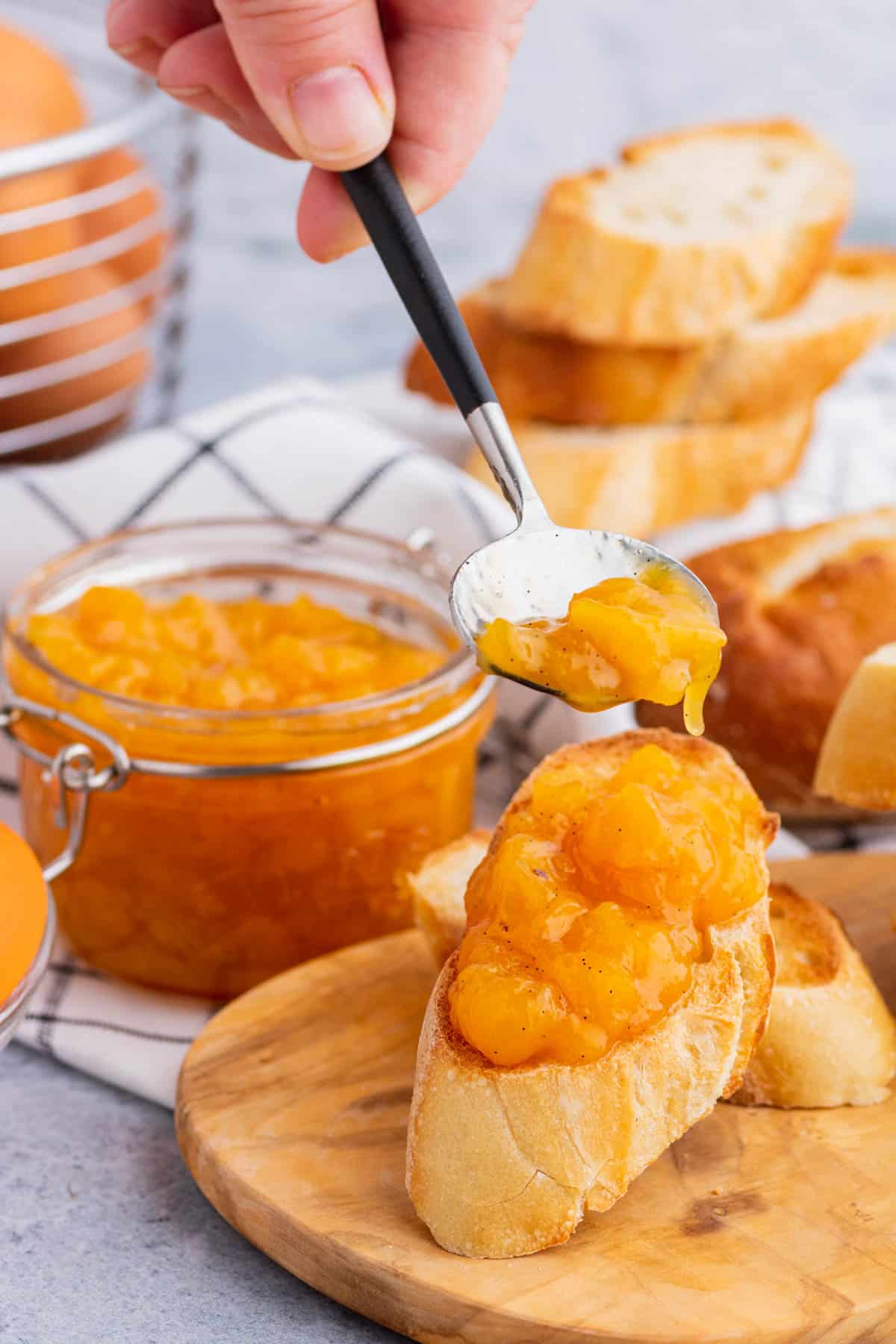 A hand holds a spoon full of Peach Freezer Jam over a slice of toast.