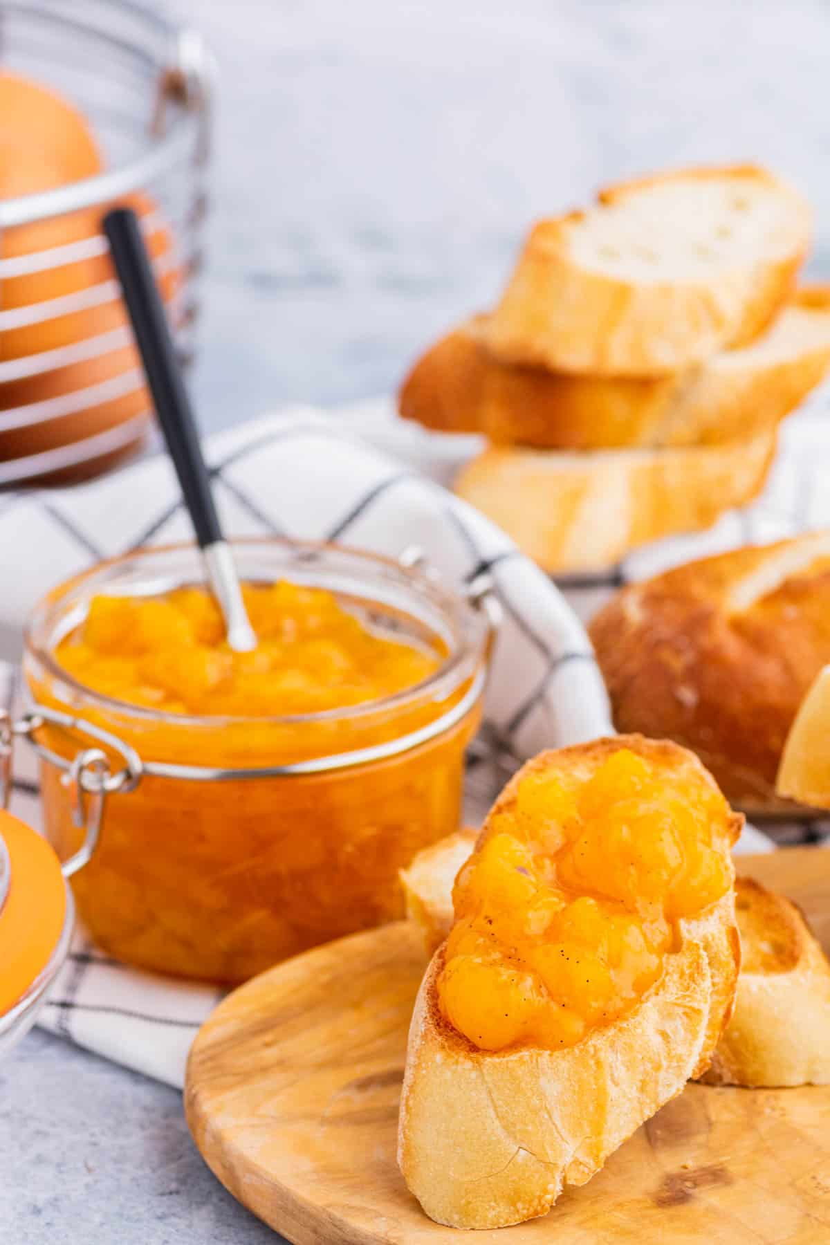 A toast covered in bright orange Peach Freezer Jam in front of a jar of the same jam.