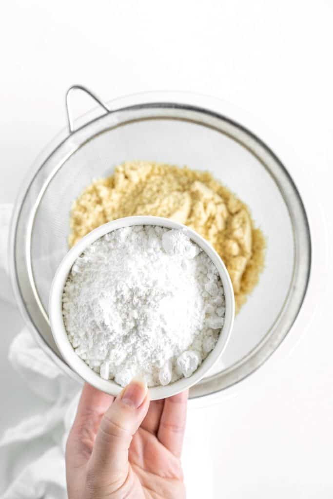 Showing icing sugar over a bowl of almond flour