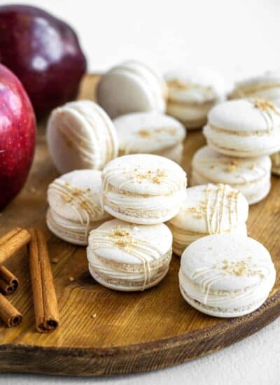 Apple Pie Macarons on a board with apples and cinnamon.