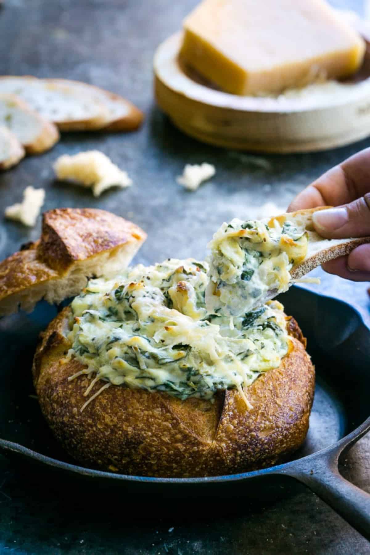 Baked spinach artichoke dip in a bread bowl in a cast iron pan