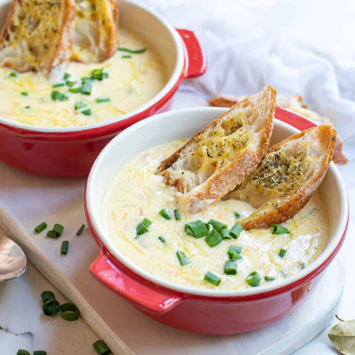 Two red bowls of beer cheese soup with toasted garlic bread. 