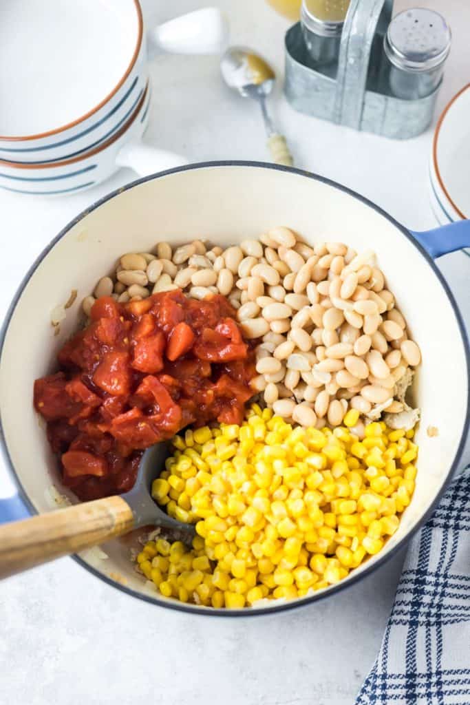 Diced tomatoes, white beans and corn in a pot over cooked chicken.