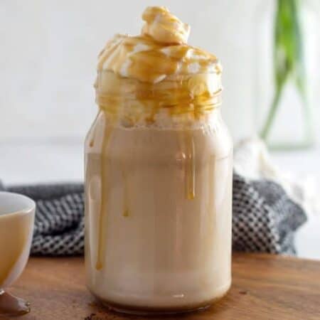 Copycat Starbucks Caramel Macchiato topped with whipped cream and caramel sauce in a jar glass