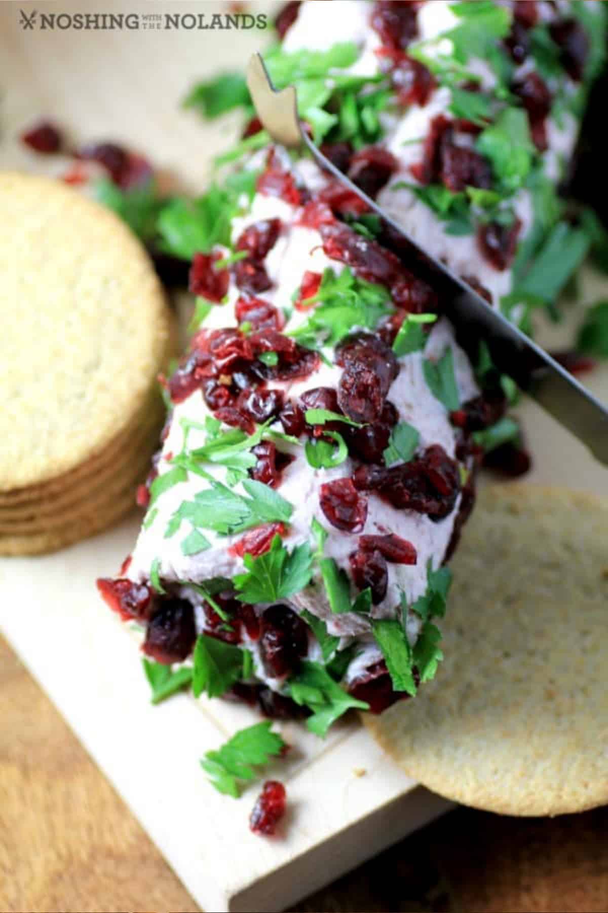 Cranberry port goat cheese log with crackers and a knife cutting into it. 