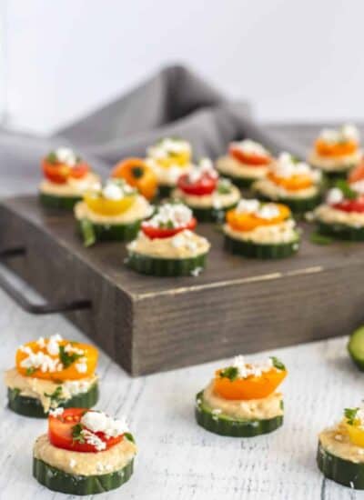 Cucumber Hummus Bites on a wooden board and ones below the board too.