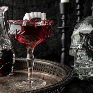 Dracula's Kiss - Halloween Cocktail on a silver tray with decanters and a glass skull on the side.
