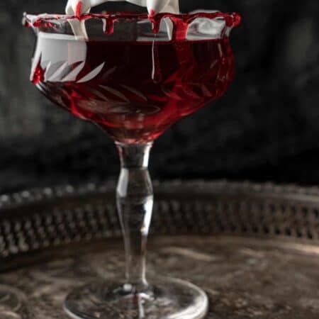 Dracula's Kiss - Halloween Cocktail on a silver tray with vampire teeth in the glass.