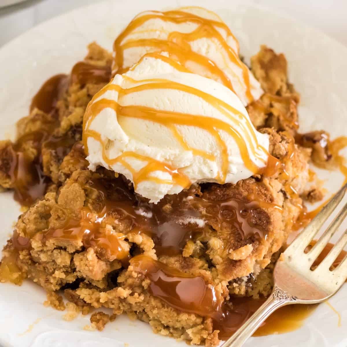 Square photo of apple dump cake with ice cream and caramel sauce. 