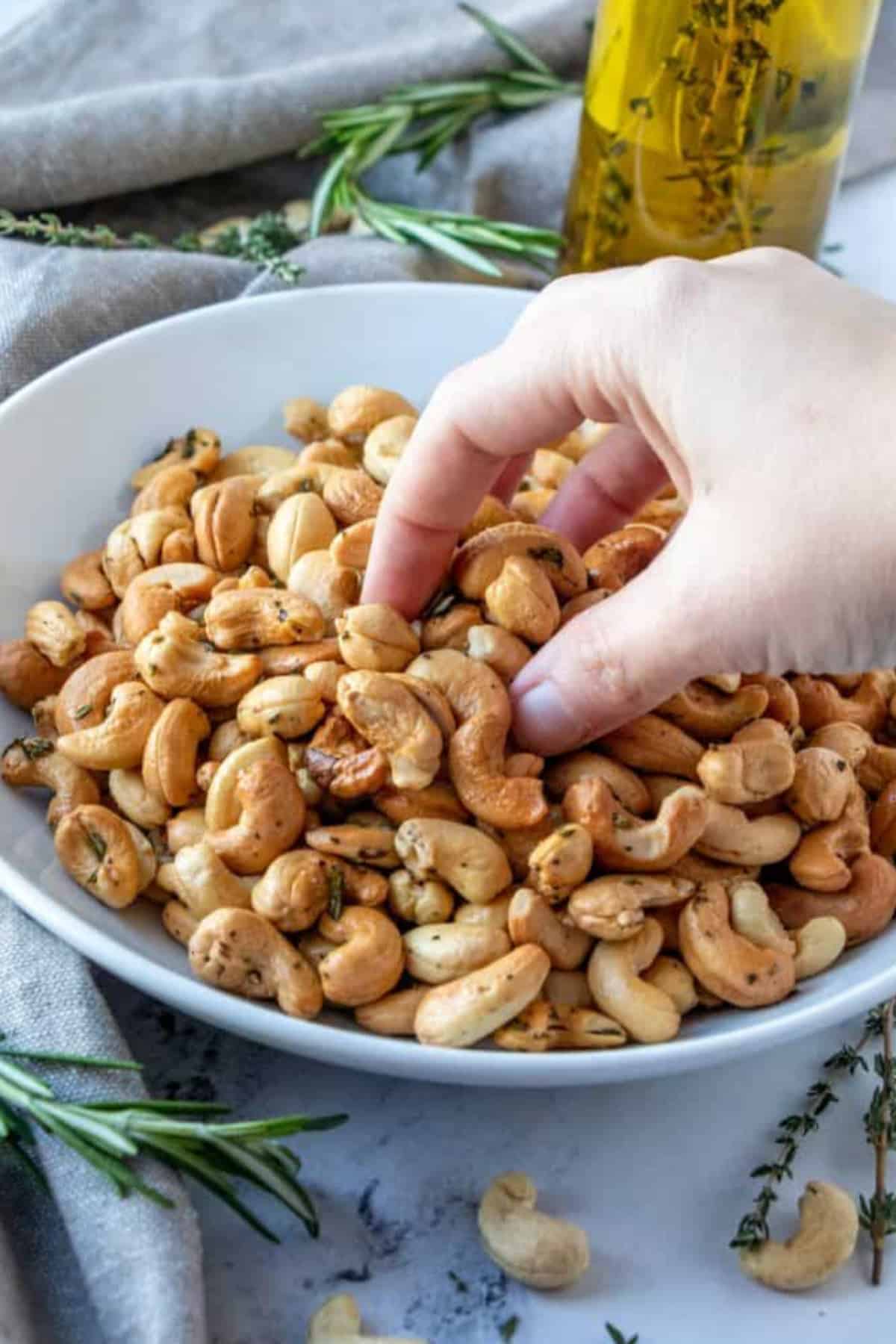 A hand grabbing herb roasted cashews from a bowl