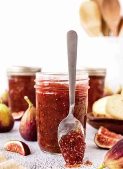 Fig jam on a spoon resting up against a jar of fig jam