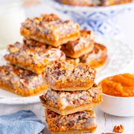 Pecan Magic Pumpkin Bars stacked in front on each other and on a plate in the background.