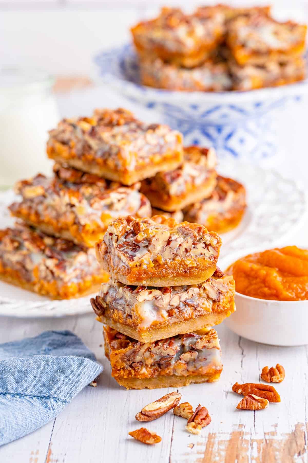 Pecan Magic Pumpkin Bars stacked in three with more in the background and a bowl of pumpkin pie filling at the side. 