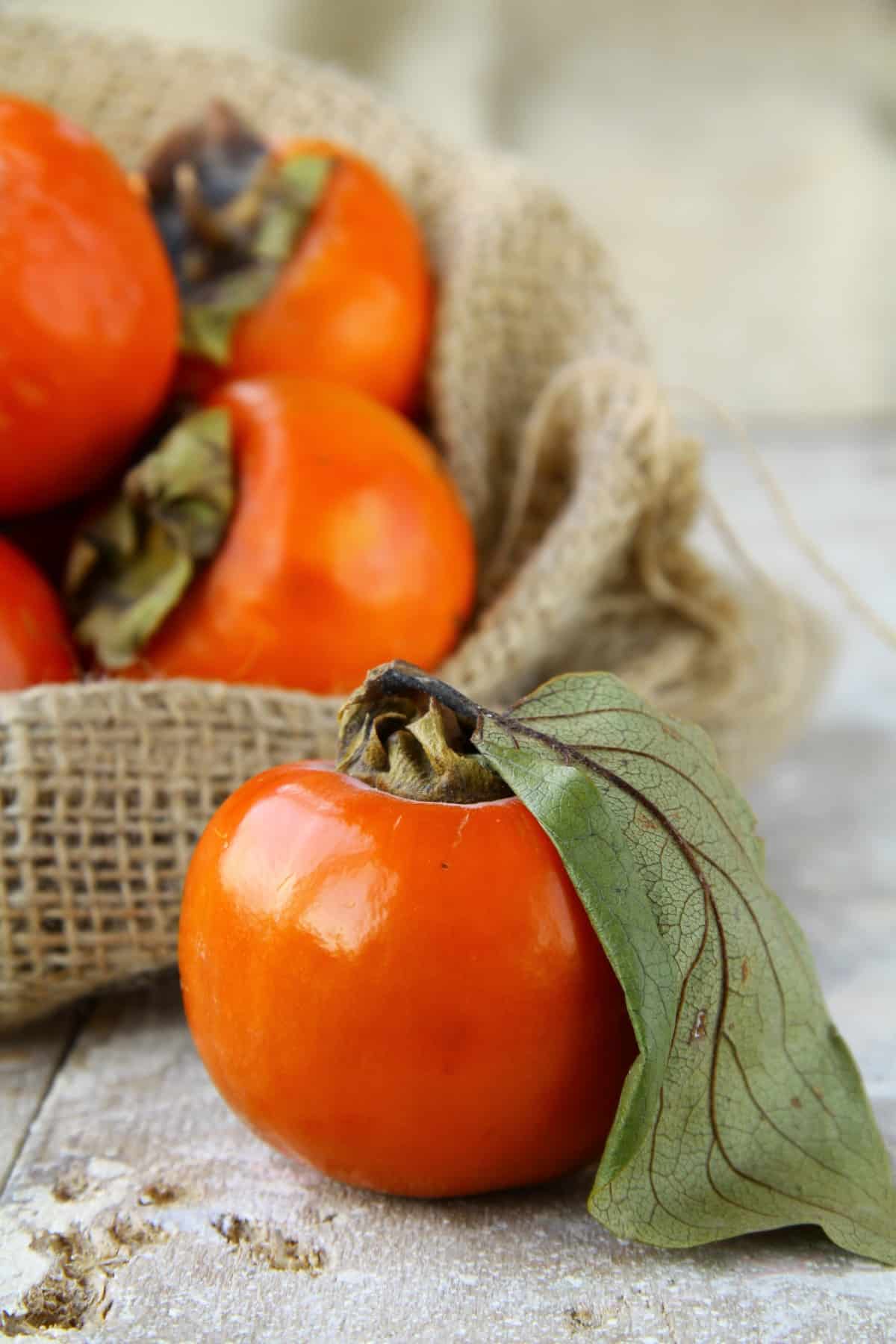 Persimmon sitting on a counter with a large leaf still attached. 