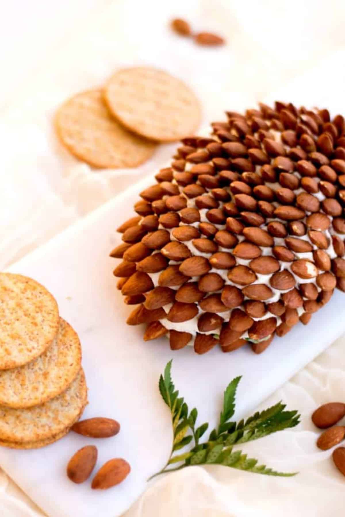 Pine cone cheese ball on a white cutting board with crackers
