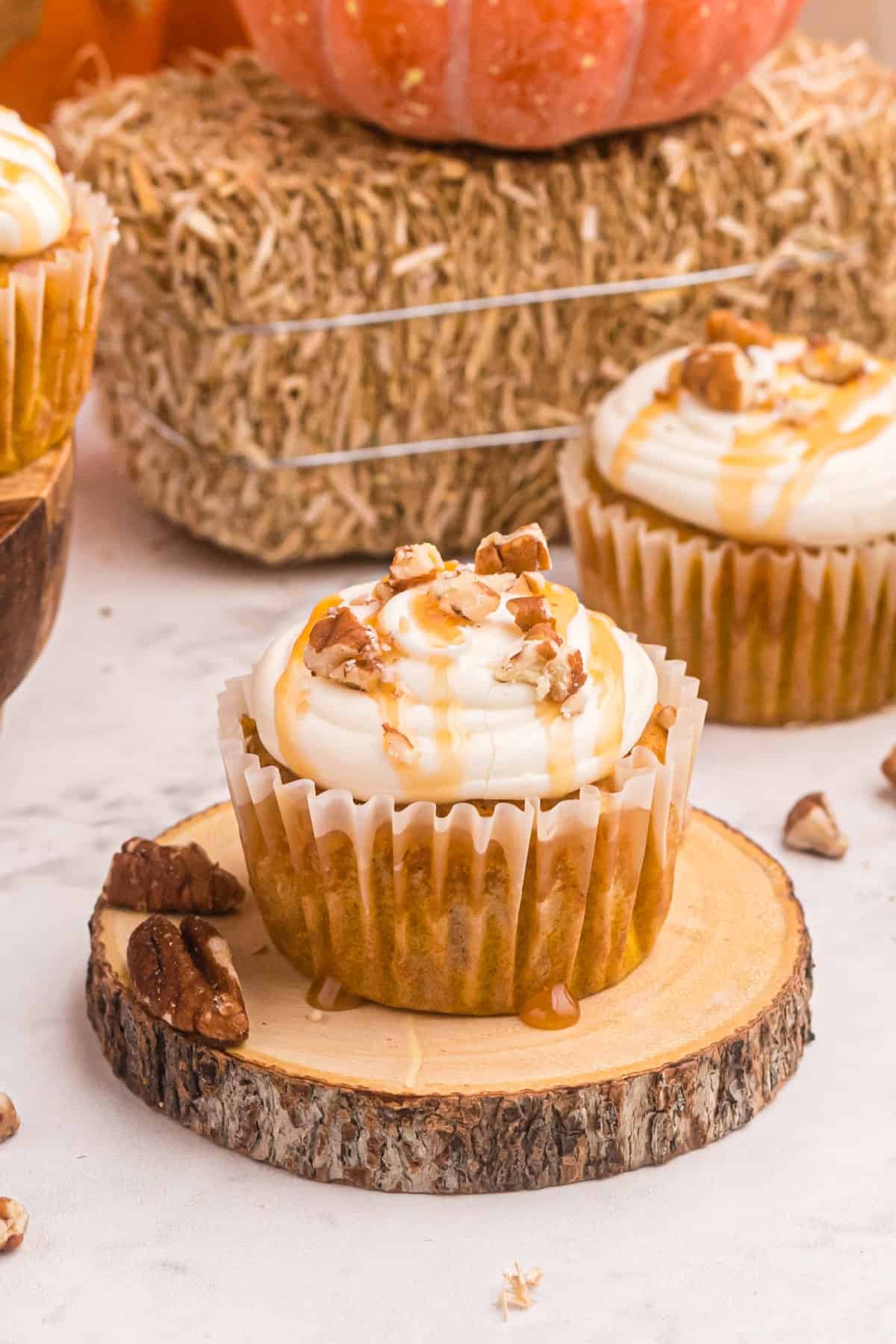 Pumpkin Cupcakes with cream cheese frosting on a wooden board on counter with hay in the background