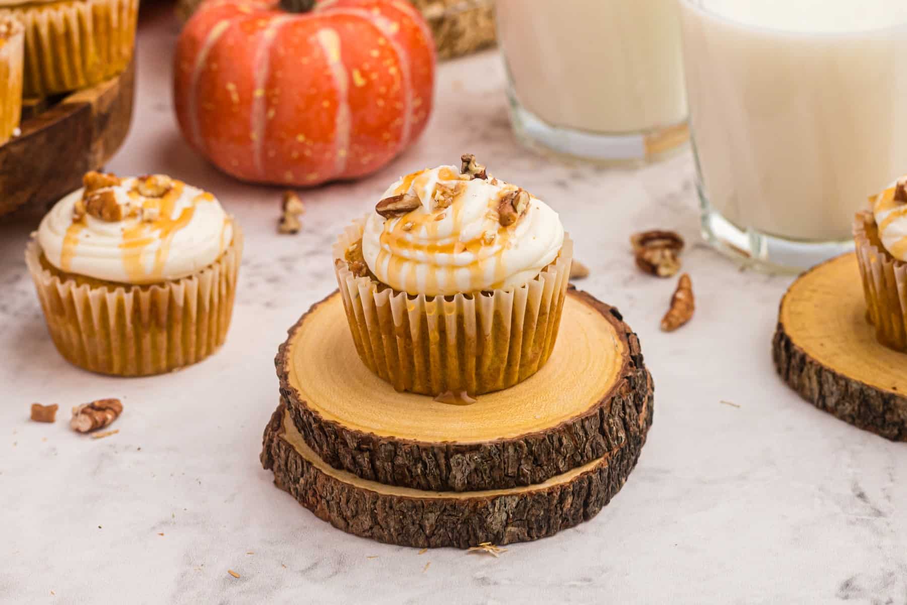 Horizontal shot of pumpkin cupcakes on stacked wooden boards with glasses of milk and a small ornamental pumpkin