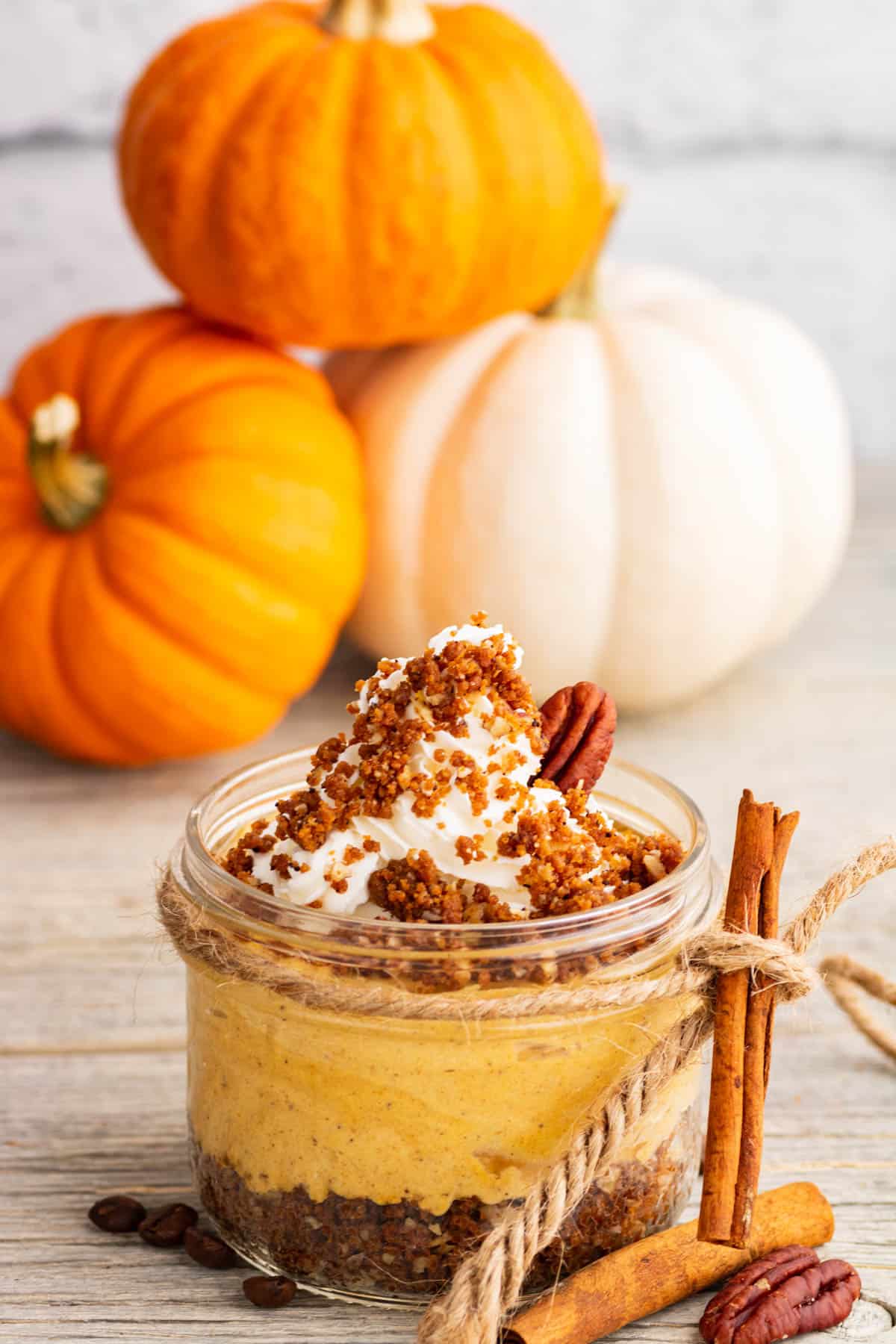 An individually sized Pumpkin Delight dessert topped with gingersnap crumbs and pecans sits amongst decorative pumpkins.