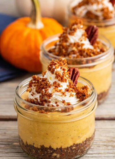 An orange pumpkin sits beside three individually sized Pumpkin Delight desserts topped with gingersnap crumbs and pecans.
