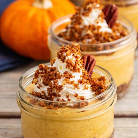 An orange pumpkin sits beside three individually sized Pumpkin Delight desserts topped with gingersnap crumbs and pecans.