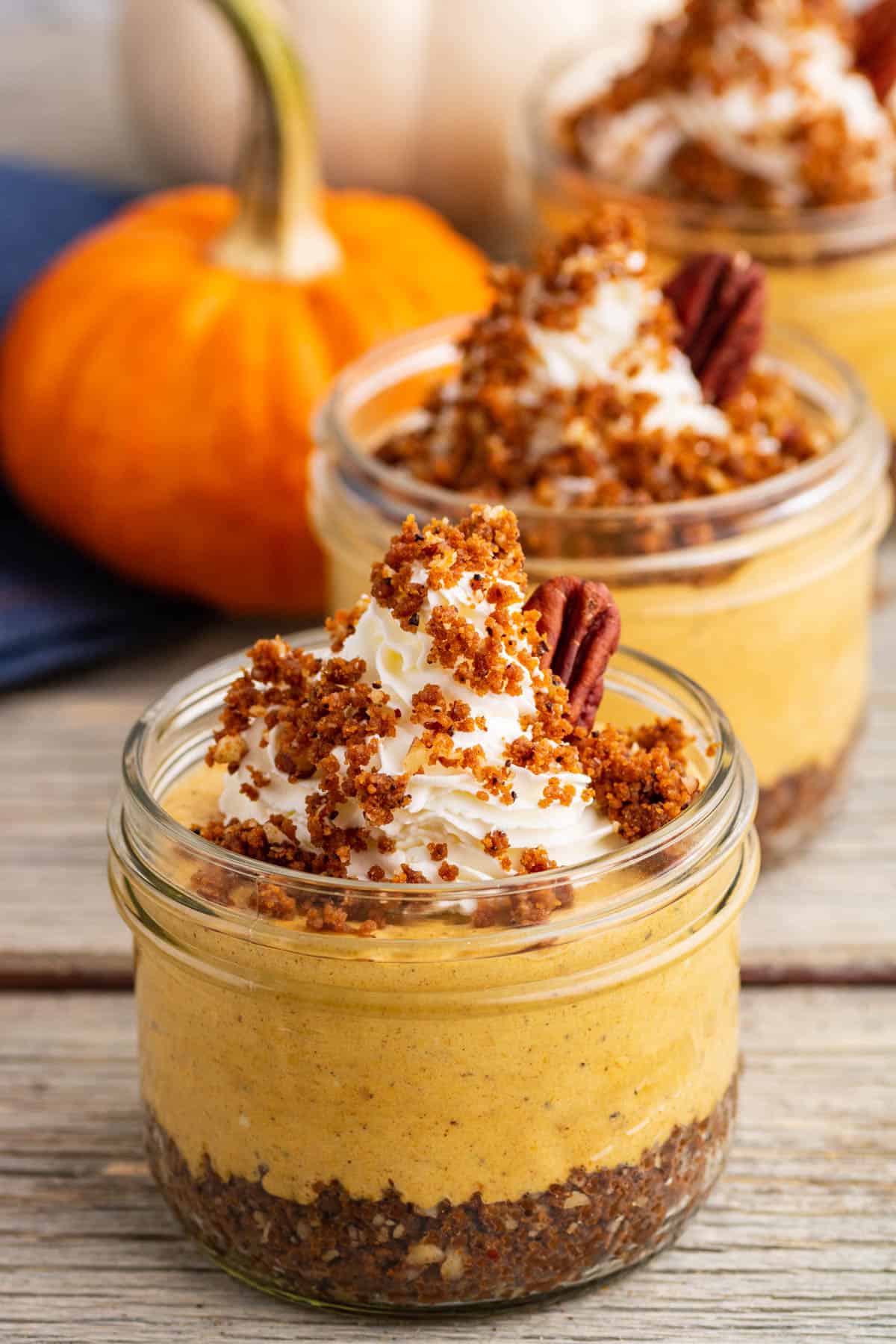 An orange pumpkin sits beside three individually sized Pumpkin Delight desserts topped with gingersnap crumbs and pecans. 