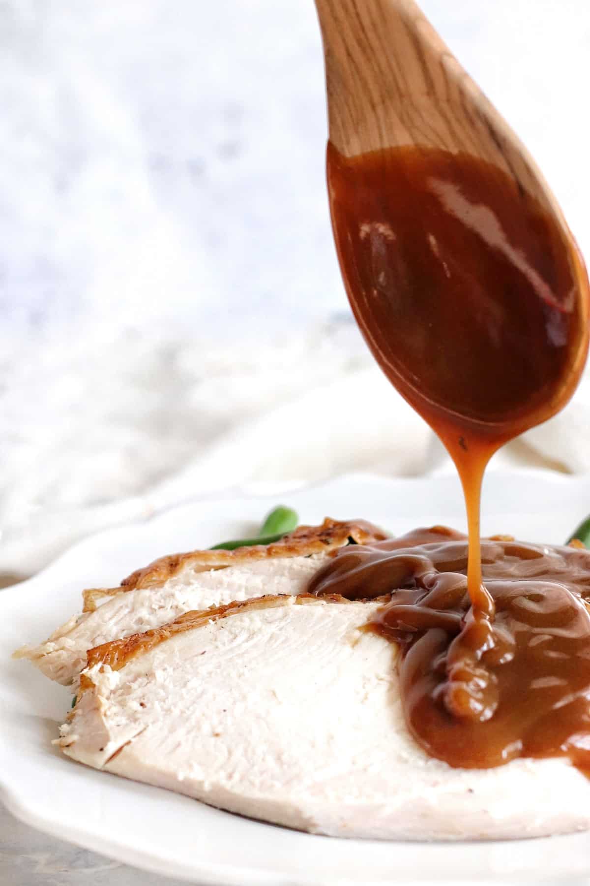 Pouring rich brown gravy from a wooden spoon onto sliced air fryer turkey breast.