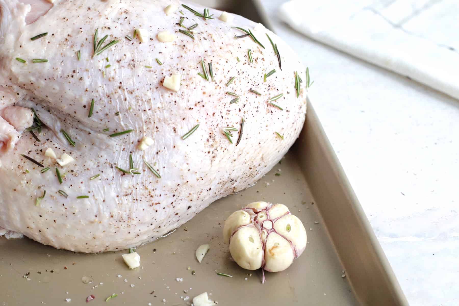 Raw turkey breast on a baking sheet with a head of garlic