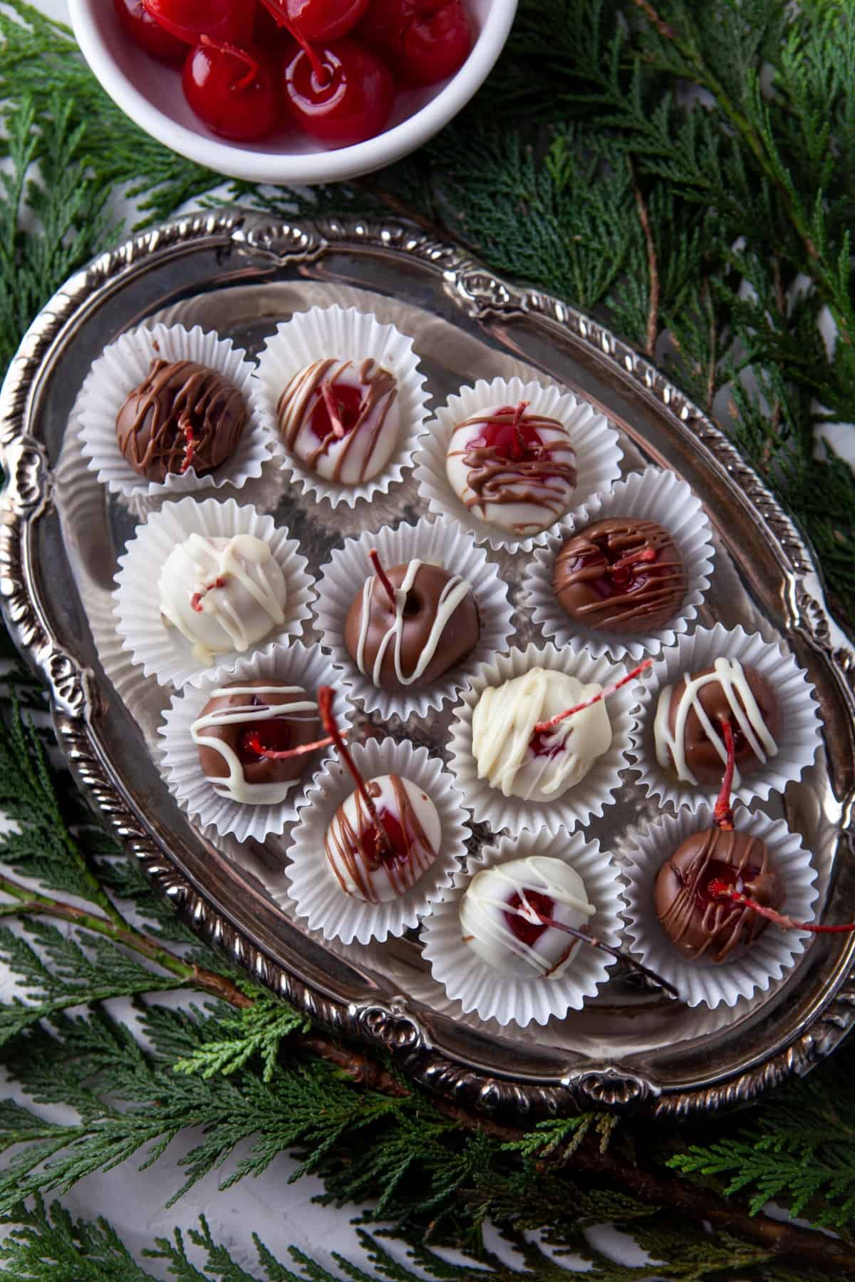 Overhead of a tray of Grand Marnier Chocolate Cherries in paper cups on evergreens. 