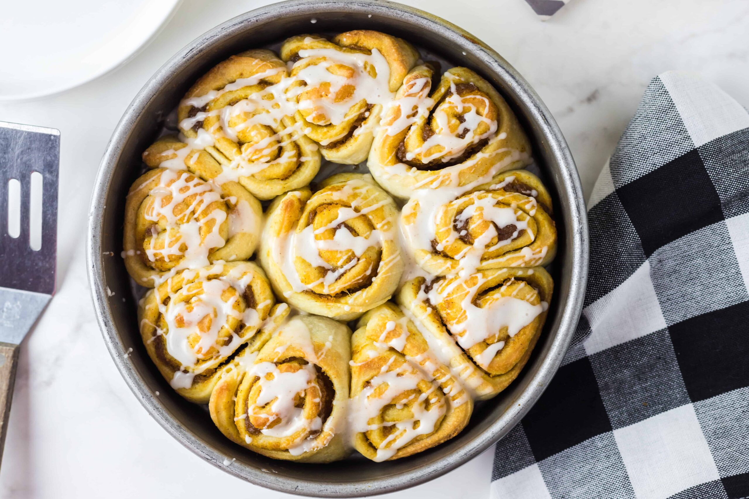 Overhead shot of rolls in a round baking pan with a spatula at the side. 