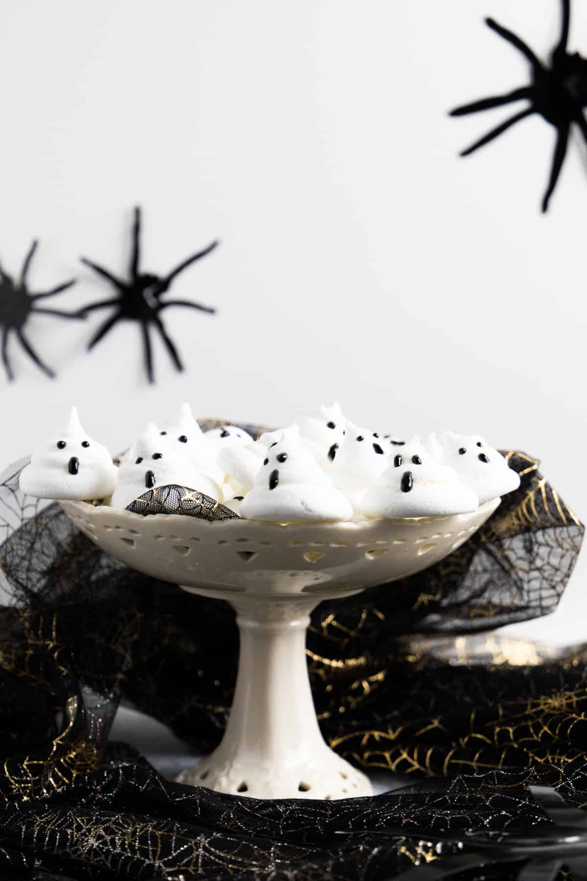 Side view of a cake stand with ghost meringues on it and fake spiders in the background