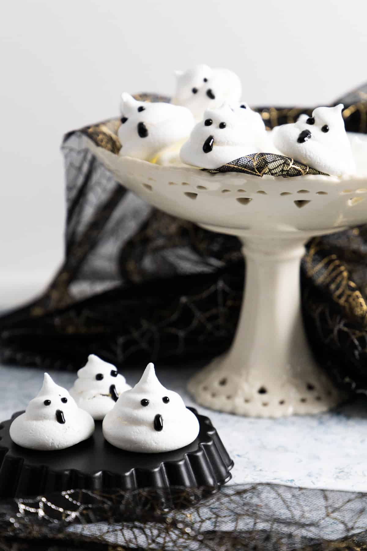 Side view of a cake stand with ghost meringues and a few on a black mold on the table. 