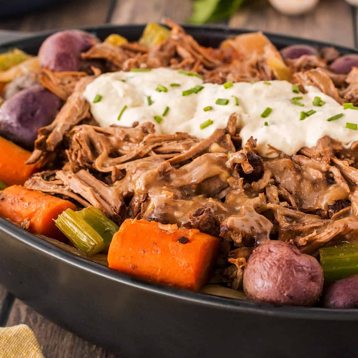 Slow Cooker Roast Beef with Potatoes and Carrots topped with horseradish sauce in a serving dish. 