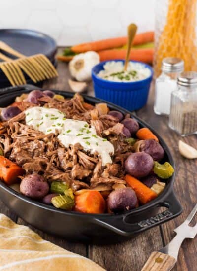 Slow Cooker Roast Beef with Potatoes and Carrots served in dish with horseradish sauce on top.