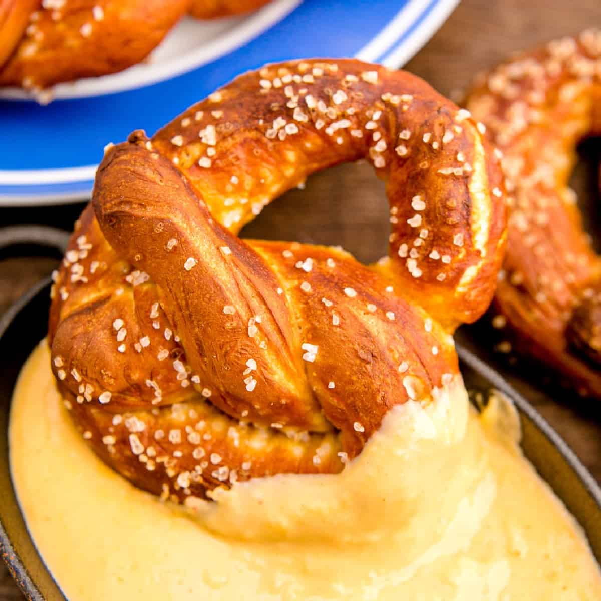 A soft pretzel dipping in a cheese dip. 