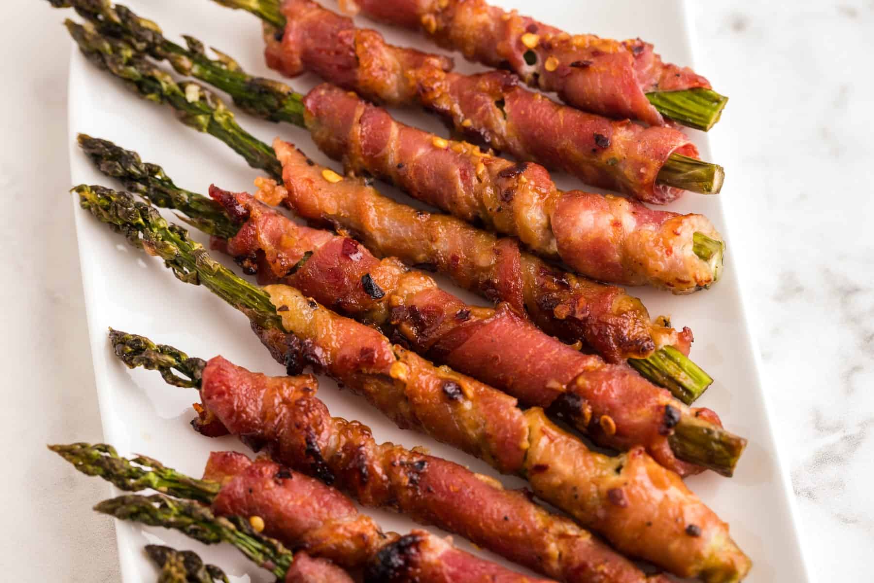 Bacon Wrapped Asparagus on a white platter, horizontal photo. 