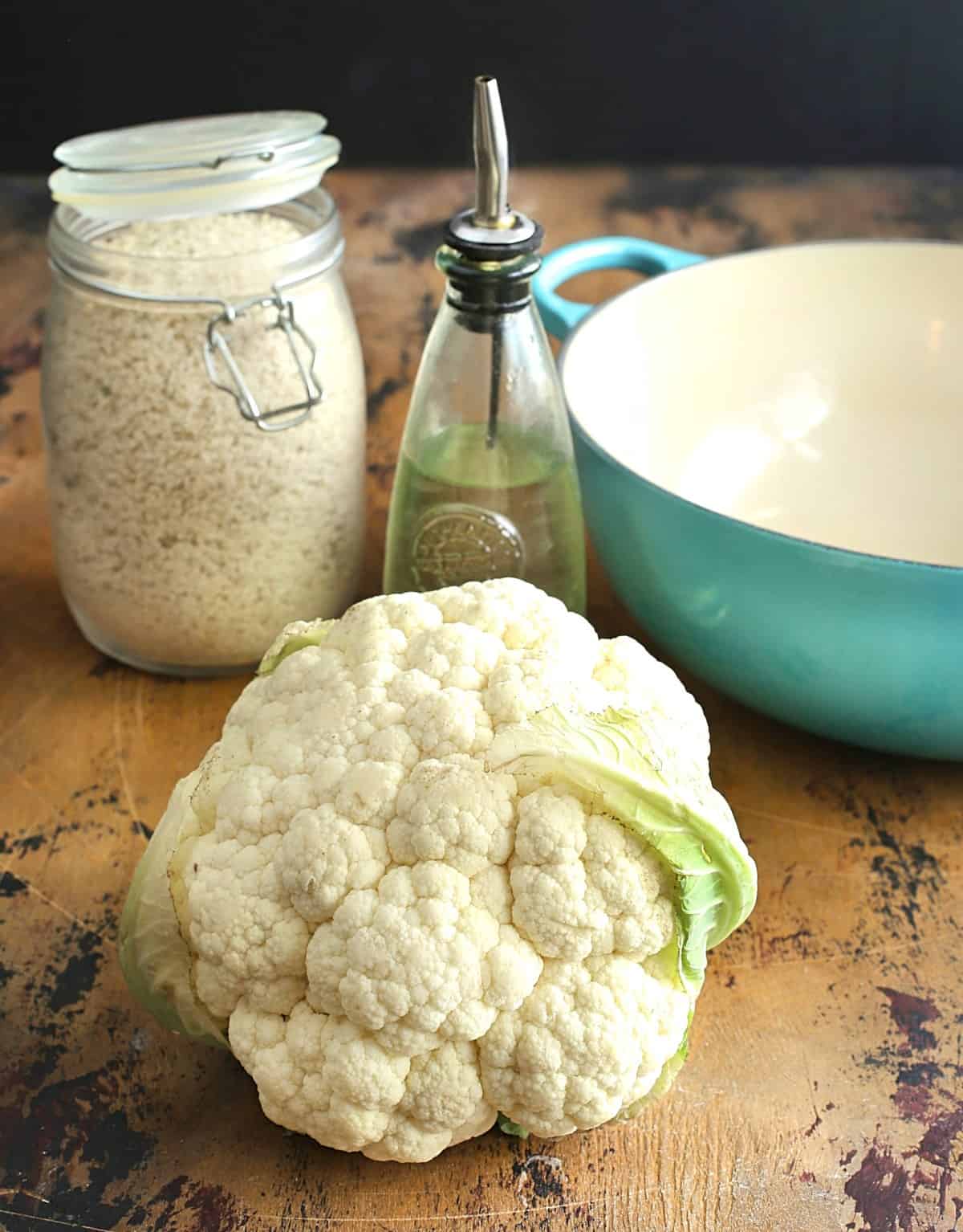 Cauliflower, oil in a bottle, bread crumbs in a jar and a blue skillet