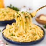 Taking a large forkful of linguini alfredo from a blue plate