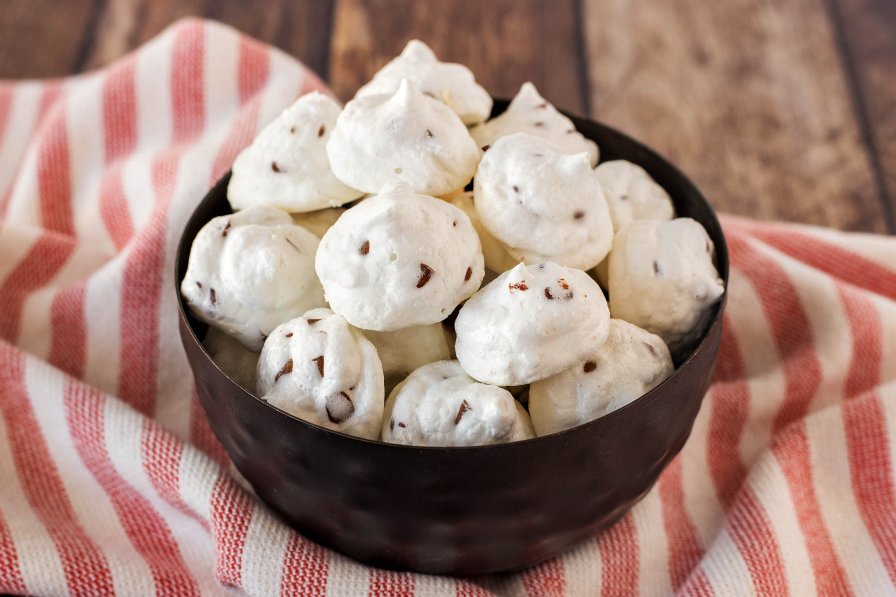 Mini chocolate chip meringue cookies in a bowl on a striped tea towel.