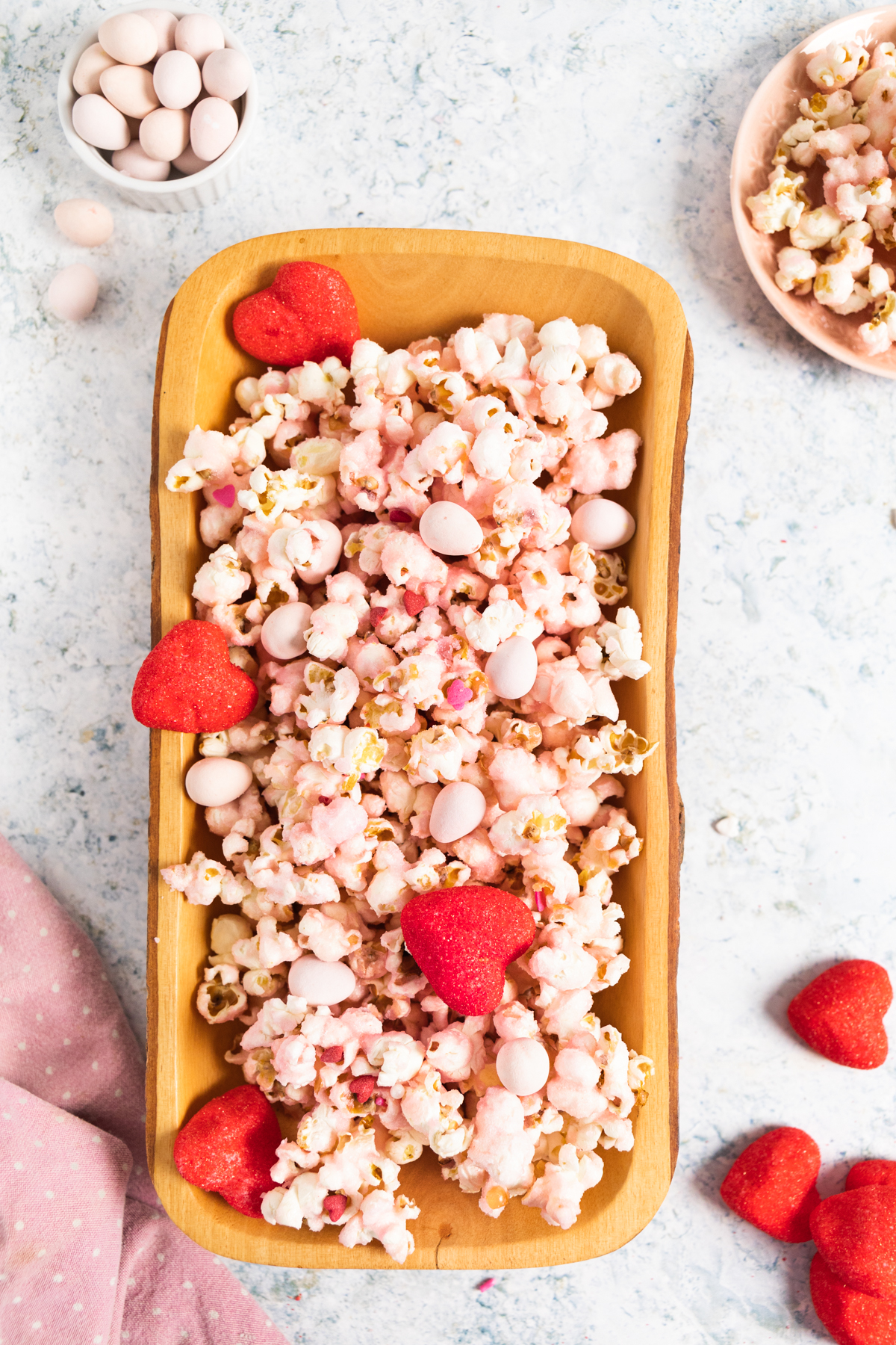 top view of pink popcorn in a wood rectangular plate and some popcorn around with heart shape marshmallows