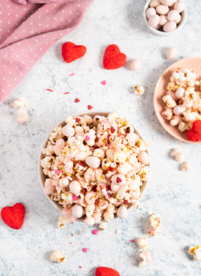 top view of pink popcorn in a bowl and some popcorn around with heart shape marshmallows
