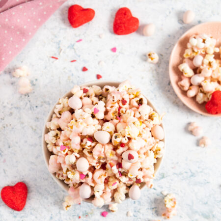top view of pink popcorn in a bowl and some popcorn around with heart shape marshmallows