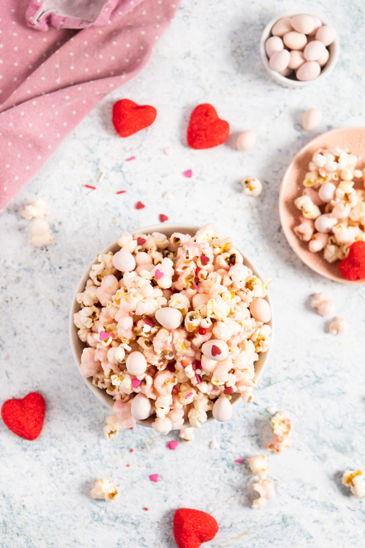 top view of pink popcorn in a bowl and some popcorn around with heart shape marshmallows