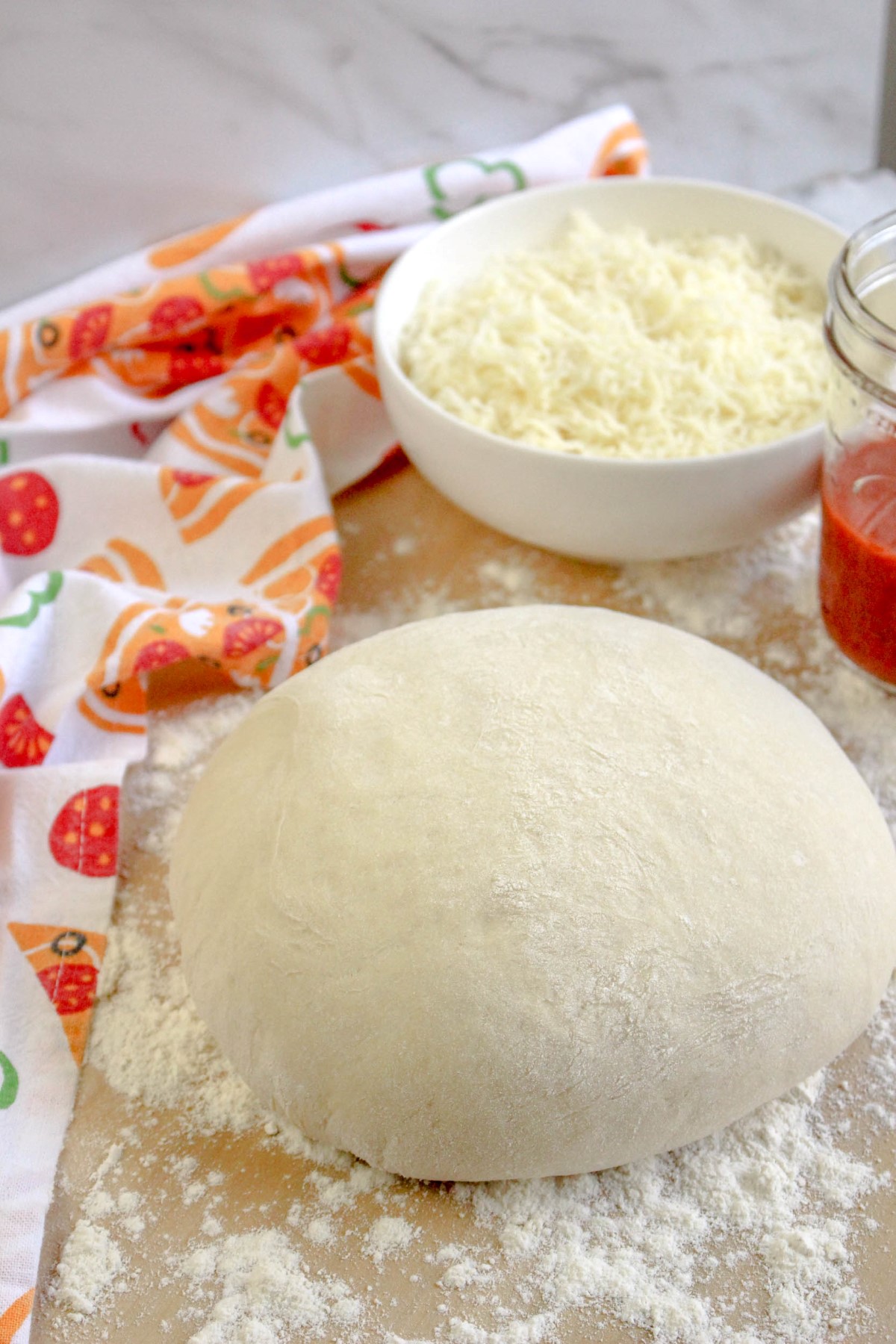 Pizza dough resting on a floured wooden board with grated cheese and tomato sauce.