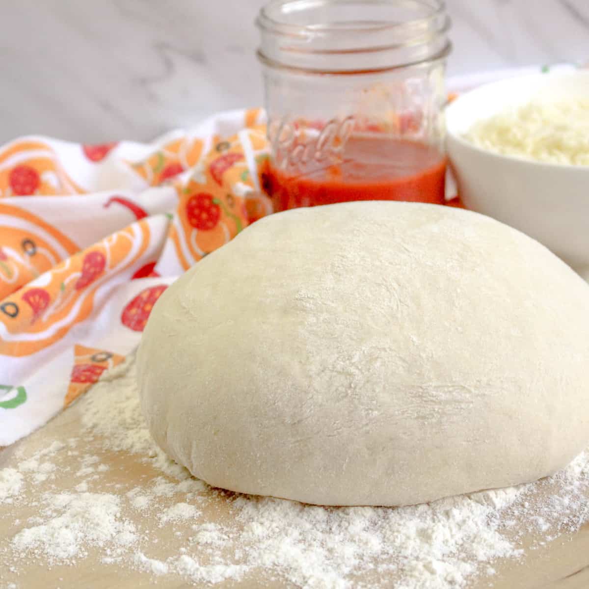 Front view of Bread Machine Pizza Dough on a floured counter with sauce and mozzarella in the background