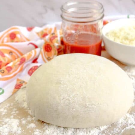 Pizza dough resting on a floured wooden board with grated cheese and tomato sauce.